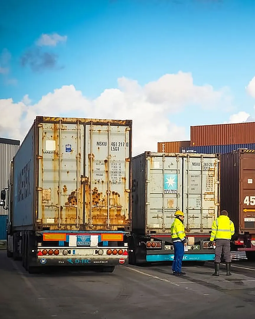 Trucks and port crew in hi-vis jackets beside loaded shipping containers